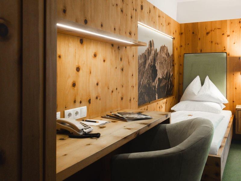 Gezellige hotelkamer met houten wanden, eenpersoonsbed, bureau en fauteuil.