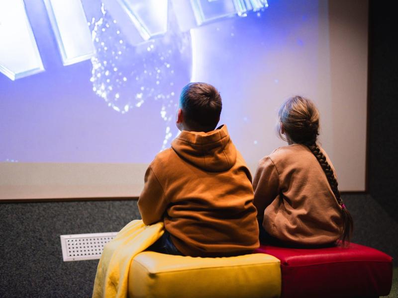 Twee mensen kijken naar een groot verlicht scherm in een donkere kamer.