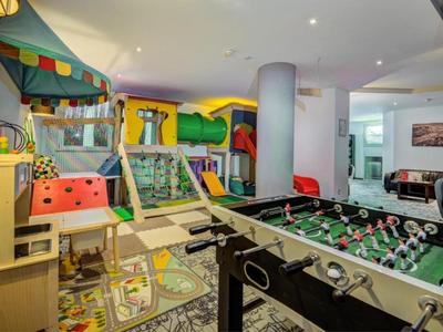 Sala de juegos infantil con futbolín, túnel de juego y juguetes coloridos bajo luz intensa.
