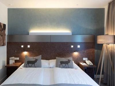 Habitación de hotel moderna con cama doble, mesas de noche y lámpara de pie junto a la ventana.