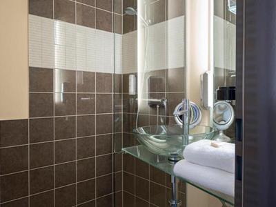 Baño moderno con azulejos marrones, lavabos de vidrio y toallero.