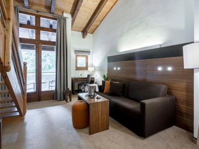 Habitación de hotel moderna con detalles de madera, sofá, escritorio, ventana y escalera.