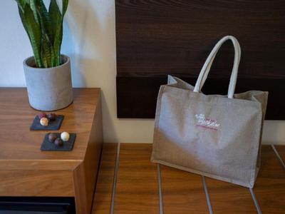 Bolsa beige colgada en una silla junto a una planta en maceta sobre una mesa de madera.