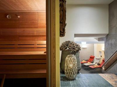 Una zona de bienestar moderna con una sauna de madera a la izquierda y una sala de relajación con tumbonas a la derecha.
