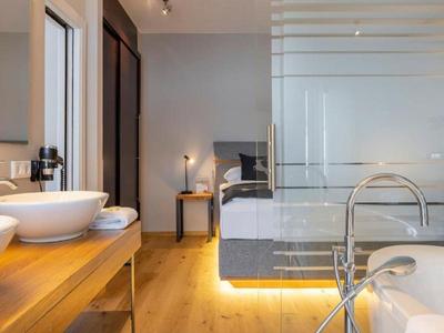 Habitación de hotel moderna con baño abierto, bañera independiente y dobles lavabos de madera.