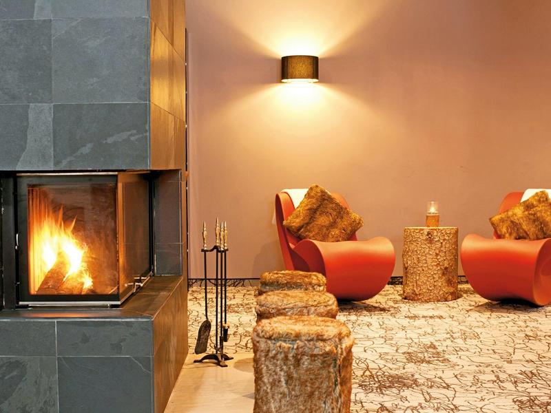 Acogedora zona de estar con chimenea moderna, dos sillones rojos y alfombra con luz cálida.
