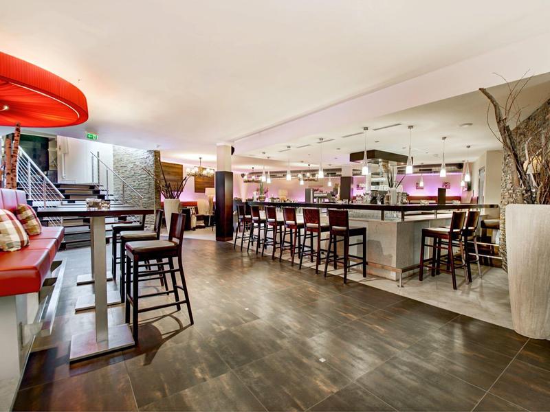 Área de bar moderna en hotel con suelo de madera oscura, taburetes y banco rojo