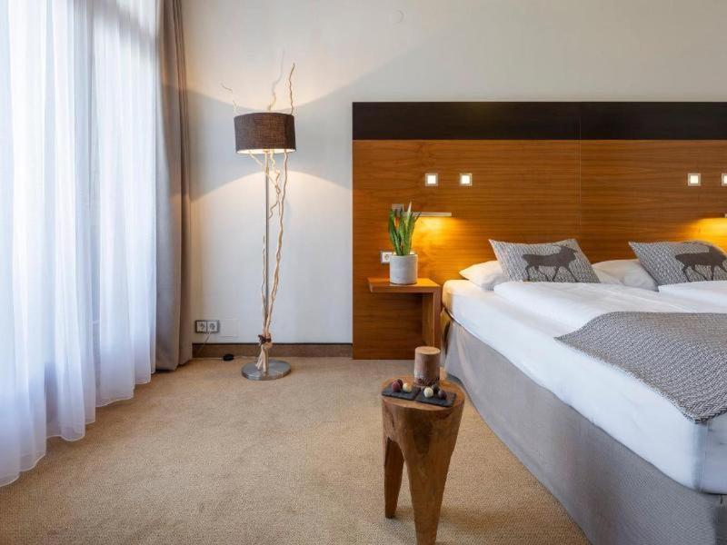 Habitación de hotel luminosa con cama grande, mesita de noche y cortinas en la ventana.