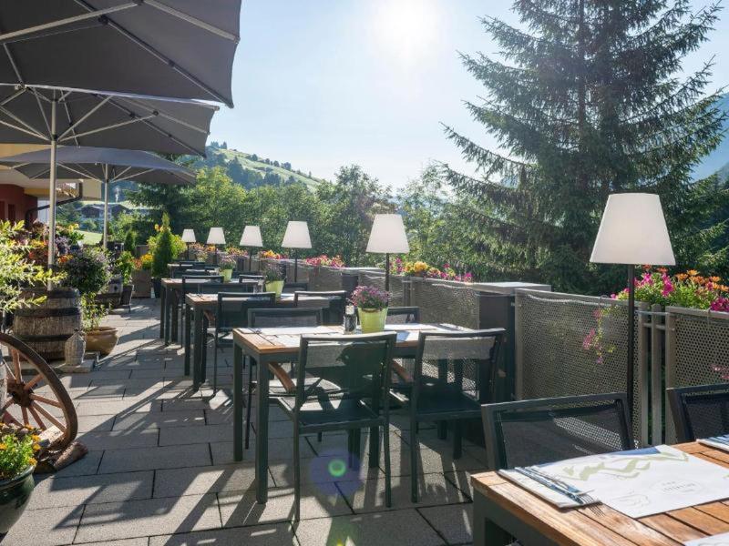 Terraza soleada con mesas y sillas, rodeada de plantas y montañas al fondo.