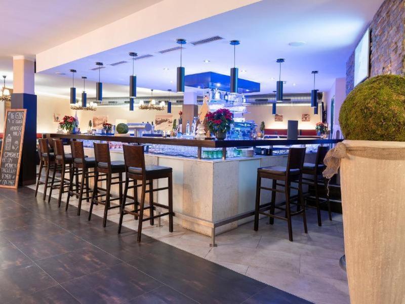 Área de bar moderna en hotel con sillas altas, mostrador iluminado y planta decorativa.