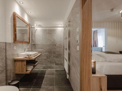 Baño moderno con lavabo doble, espejo grande y ducha a ras de suelo junto a dormitorio.