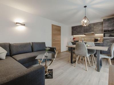 Sala y comedor modernos con sofá gris, mesa de comedor y cocina abierta de madera.