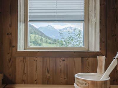 Ventana con vista a montañas y valle en sauna de madera con cubo y cucharón.