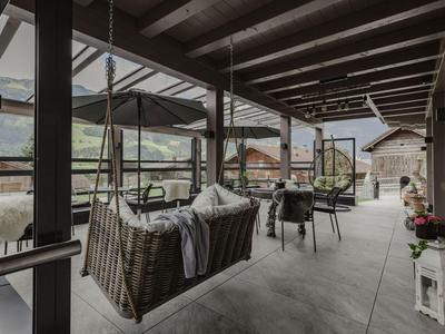 Terraza cubierta con sillas colgantes, techo de vigas de madera y vista a la montaña.