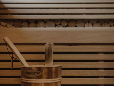 Sauna acogedora con bancos de madera y un cubo con un cucharón frente a leña apilada.