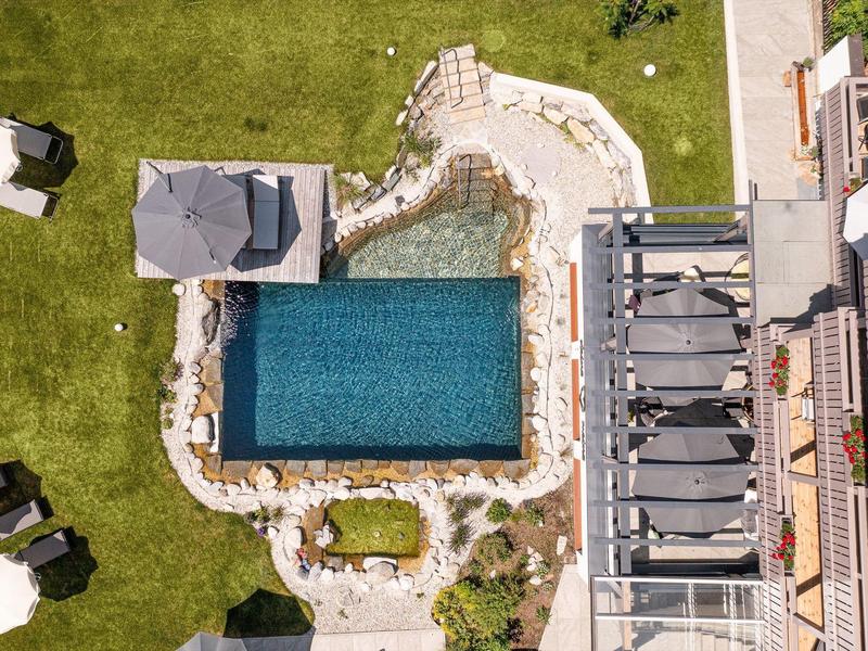 Vista aérea de una piscina rectangular en un jardín de hotel con tumbonas y césped verde.