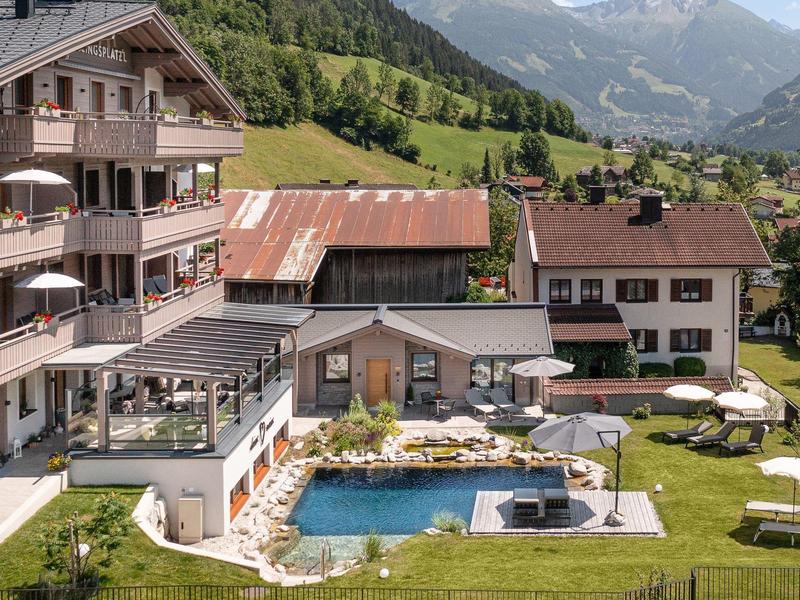 Hotel con piscina al aire libre y tumbonas en un paisaje montañoso con prados verdes.
