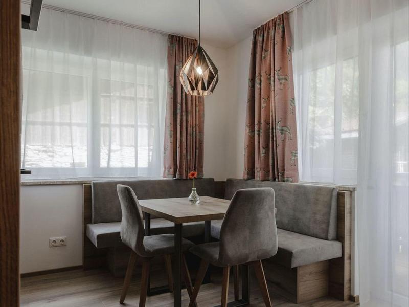 Área de comedor moderna con sofá de esquina gris, suelo de madera y lámpara colgante a la luz del día