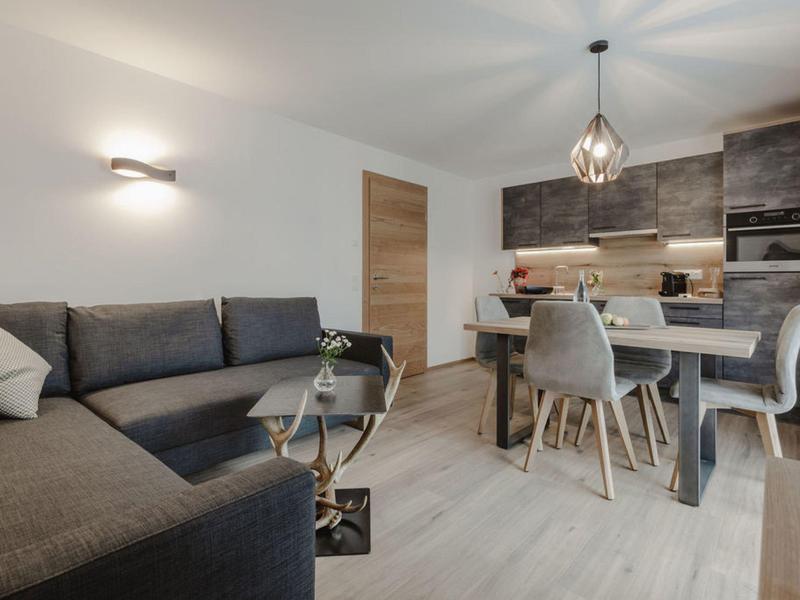 Sala y comedor modernos con sofá gris, mesa de comedor y cocina abierta de madera.