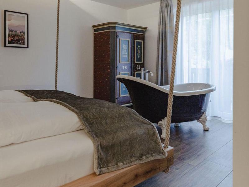 Elegante habitación de hotel con techo de madera, bañera independiente y cama acogedora.