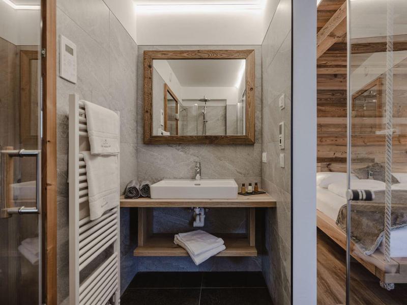 Área moderna de baño en hotel con lavabo, espejo y toallas junto a un dormitorio.