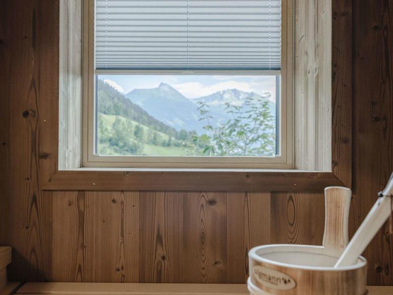 Ventana con vista a montañas y valle en sauna de madera con cubo y cucharón.