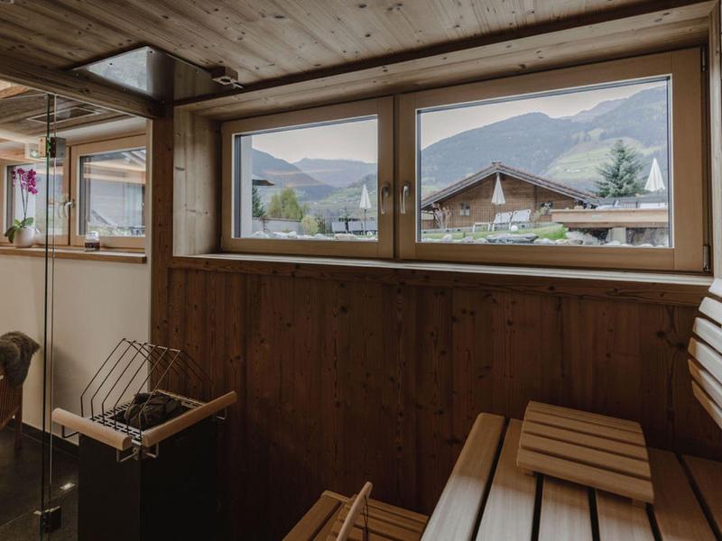 Interior acogedor de sauna con bancos de madera y grandes ventanas con vista a las montañas.