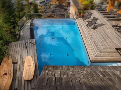 Piscina moderna con terrazza in legno e lettini in un hotel con vista sugli alberi.