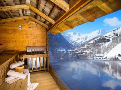 Balcone in legno con sedia e asciugamani, vista su montagne innevate e lago.