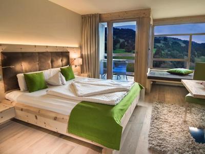 Camera d'hotel moderna con letto matrimoniale con accenti verdi, balcone con vista sulle montagne.