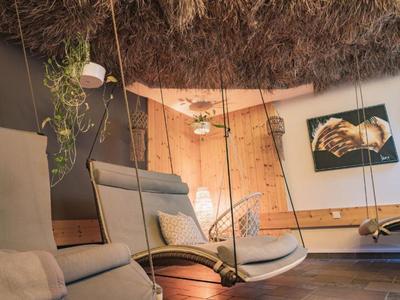 Area lounge accogliente con sedie a dondolo sotto un tetto di paglia in un hotel.