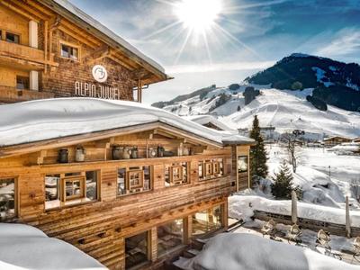 Chalet in legno con tetto innevato davanti a uno sfondo montano e sole splendente