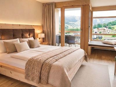Habitación de hotel moderna con cama grande, muebles de madera y balcón con vista a la montaña.