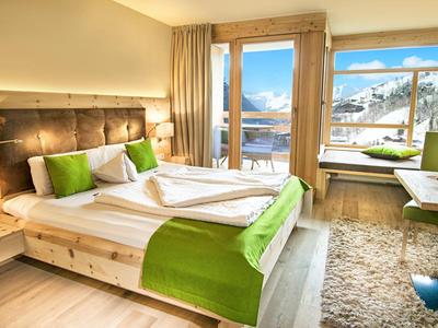 Habitación de hotel luminosa con cama doble, detalles verdes y vista a montañas nevadas.
