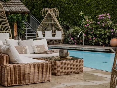 Área exterior moderna con muebles de ratán y piscina en un jardín de hotel.