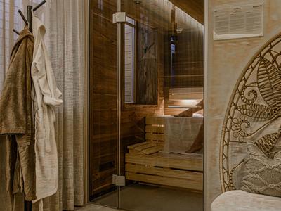 Entrada acogedora de sauna con puerta de vidrio, batas y una silla decorativa en un hotel.