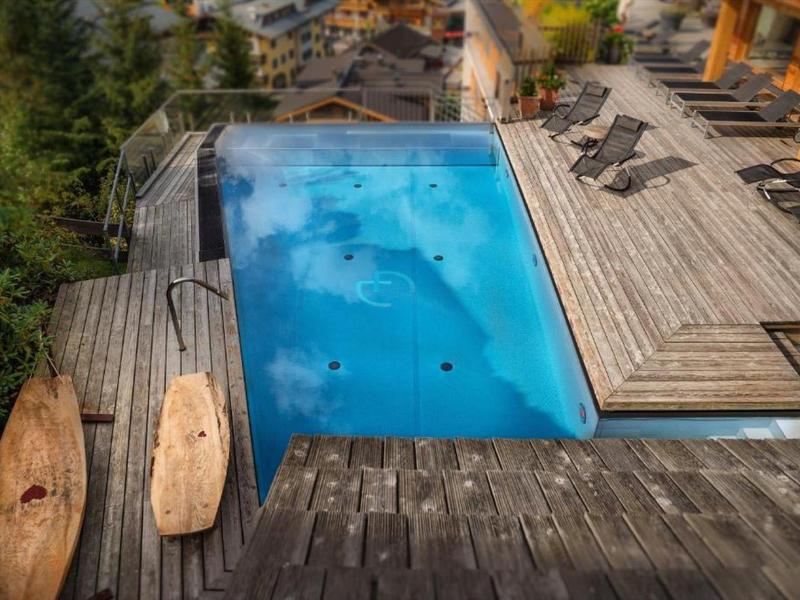Piscina moderna con terrazza in legno e lettini in un hotel con vista sugli alberi.