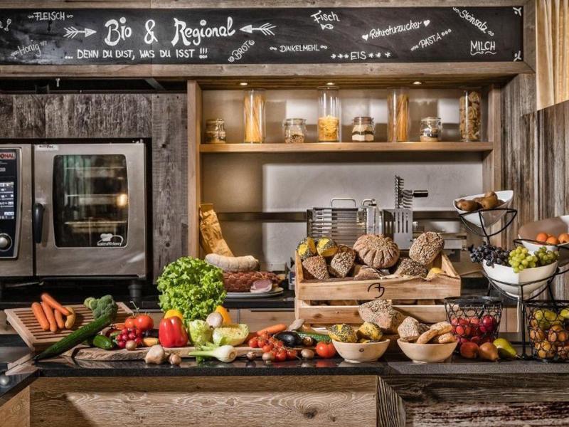 Verdure fresche, pane e prodotti da forno su un buffet rustico con forno sullo sfondo.