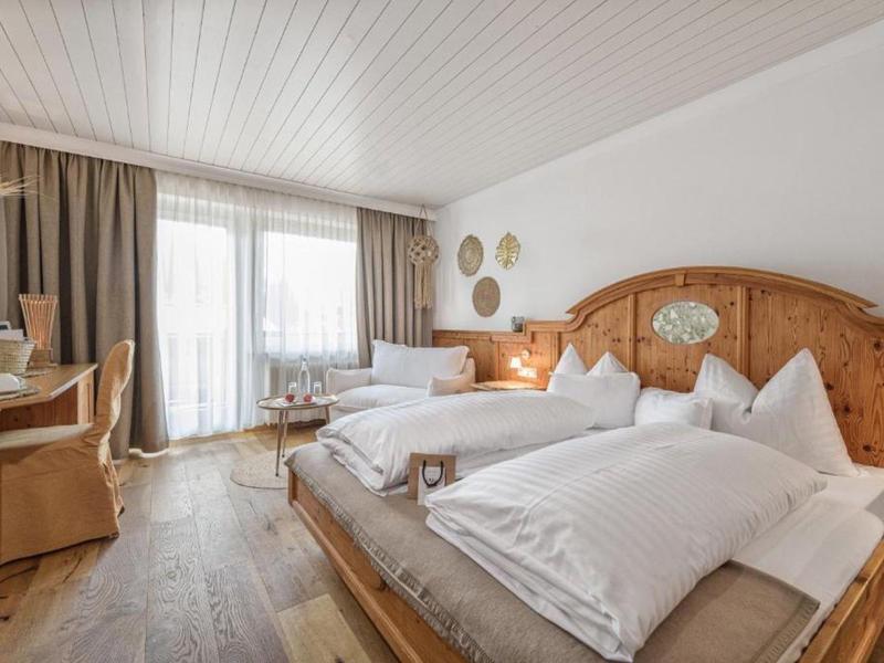 Camera d'hotel luminosa con letto matrimoniale, pannellature in legno e scrivania vicino alle finestre del balcone.