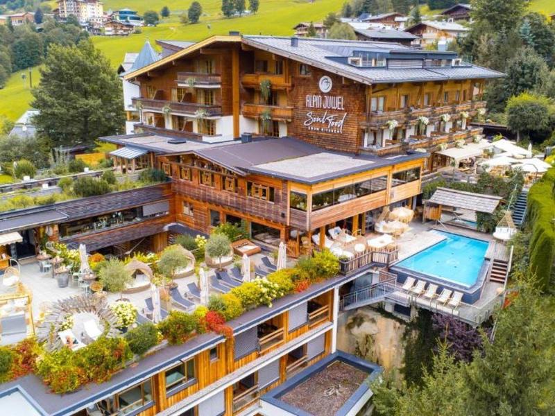 Grande hotel di montagna con più piscine e molta vegetazione in un ambiente alpino.