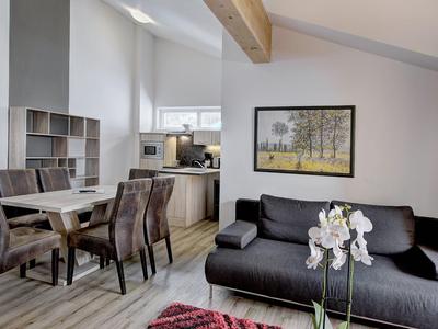 Modern eingerichtetes Wohnzimmer mit Sofa, Esstisch und offener Küche unter schiefer Decke.