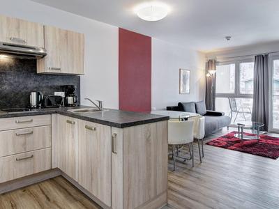 Modern kitchen and living room with wooden floor, light furniture, and red rug
