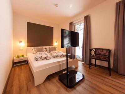 Modern eingerichtetes Hotelzimmer mit Doppelbett, TV auf Ständer und Holzboden.