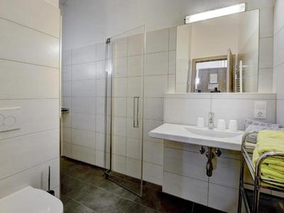 Modernes Badezimmer mit großer Dusche, weißem Waschbecken und Handtuchhalter mit grünen Handtüchern.