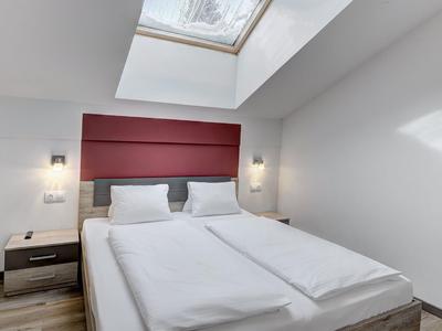 Bright hotel room with double bed under skylight and modern wooden flooring.