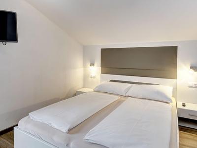 Modern hotel room with large double bed, wall lamps, and flat-screen TV on white wall.