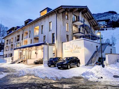 Modern hotel building with lit windows, cars parked by underground garage, snow-covered at dusk.