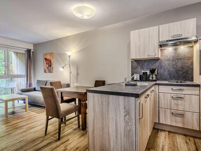 Living area with modern kitchen, dining table and chairs, light wooden floor, and window view.