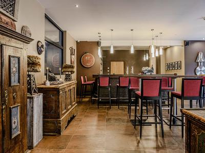 Modern hotel bar with wooden interior, red bar stools, and decorative wall art.