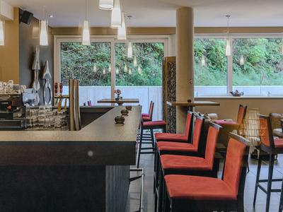 Modern hotel bar with tall orange upholstered chairs and view of green outdoor area.